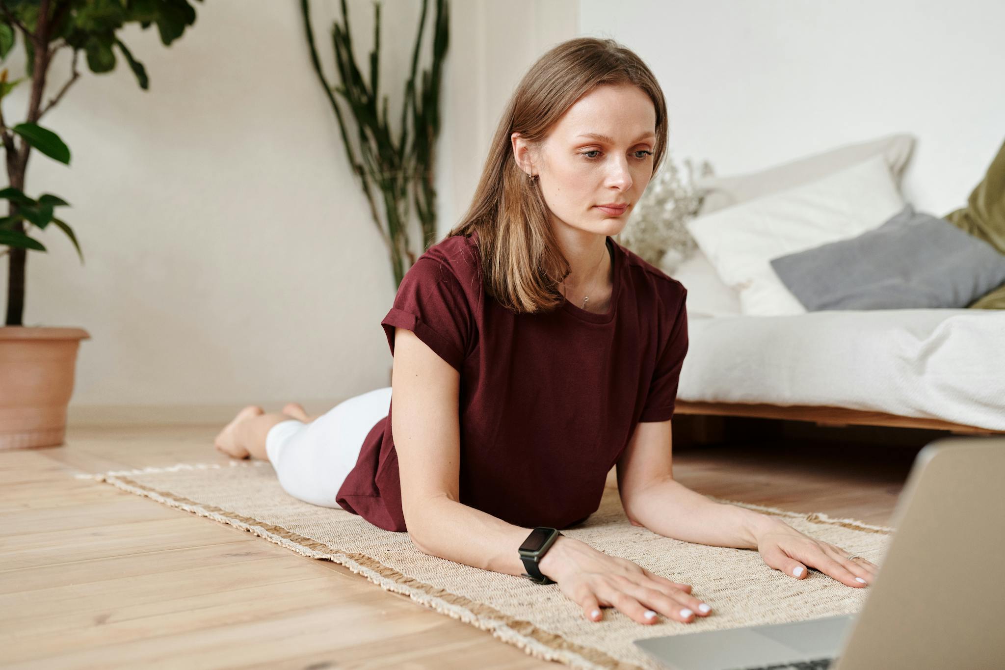 A woman balances work and wellness by practicing yoga on a mat while using a laptop indoors.